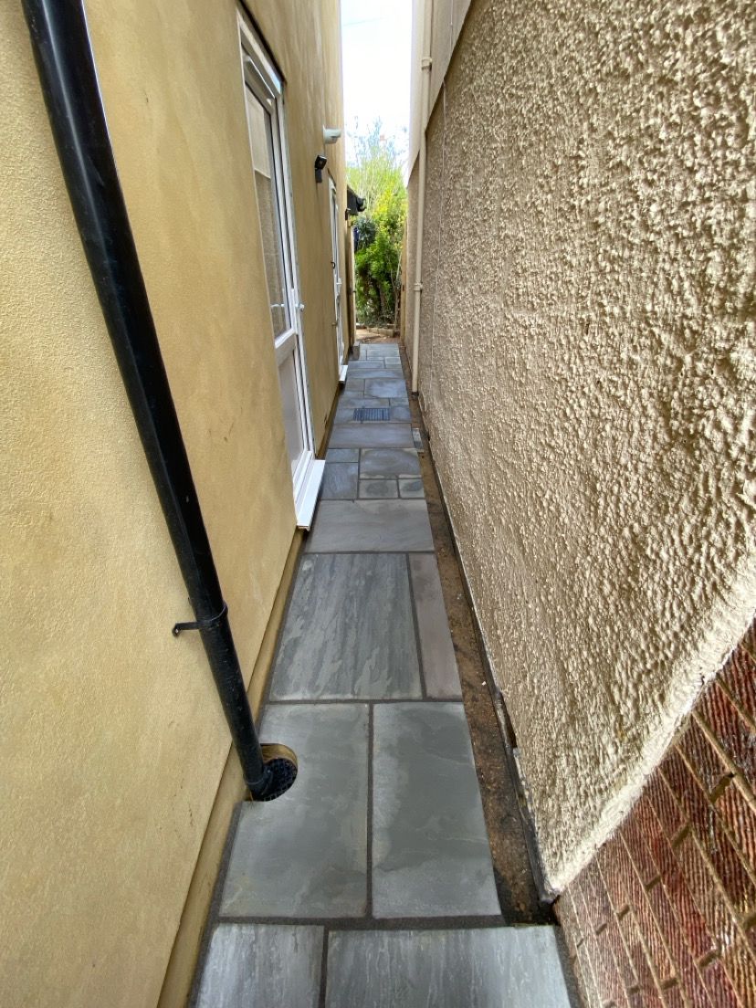 Large format grey paving slabs installed in narrow side pathway between buildings