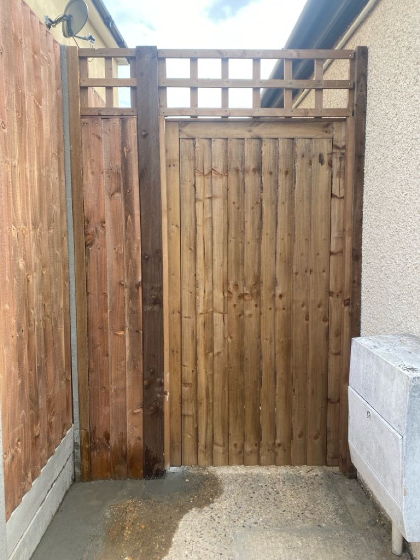 Custom wooden garden gate with decorative lattice top between fence panels